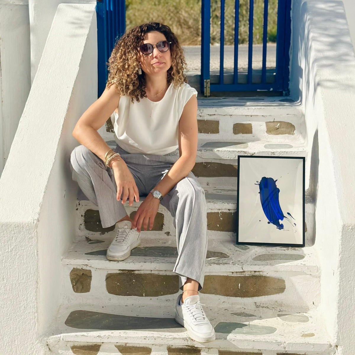 FLOR. sitzend neben ihrem Kunstwerk in Blau auf Paros in Adelfia Studios. 