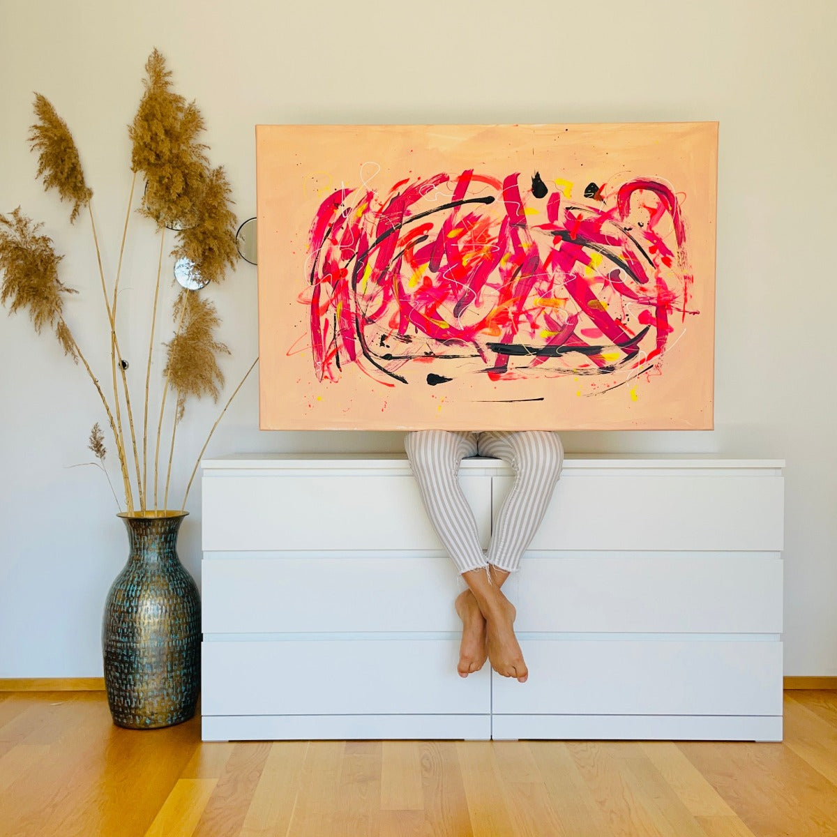 FLOR. sitzend auf der weißen Kommode mit ihrem abstrakten Kunstwerk Neon Jungle, dass für bunten Farben wie Rosa, Pink, Schwarz, Gelb nur sprüht. 